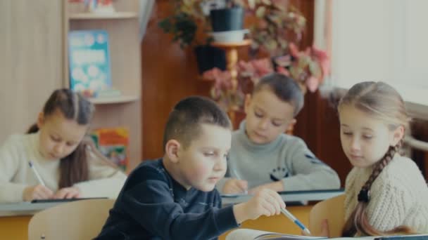 Crianças escrevem sentadas em uma mesa — Vídeo de Stock