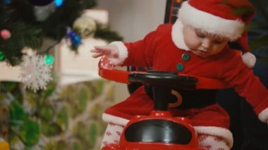 santa elbiseli küçük bir kız bir yılbaşı ağacı yakınındaki bir oyuncak araba haddeleme