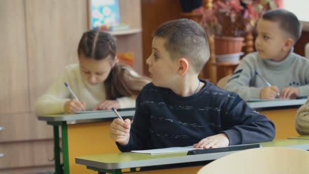 Crianças escrevem sentadas em uma mesa — Vídeo de Stock