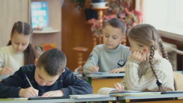 Los niños escriben sentados en un escritorio — Vídeos de Stock