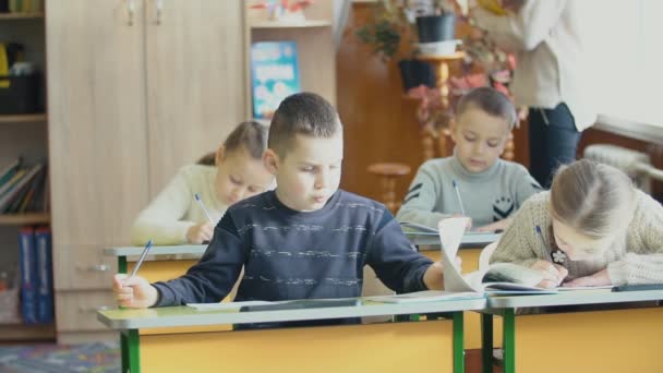 Los niños escriben sentados en un escritorio — Vídeo de stock