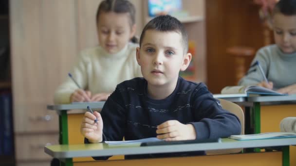 Los niños escriben sentados en un escritorio — Vídeo de stock