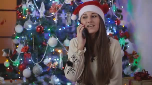 Menina com um telefone no fundo da árvore de Natal — Vídeo de Stock