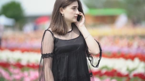 Девушка разговаривает по телефону на тюльпановом поле — стоковое видео