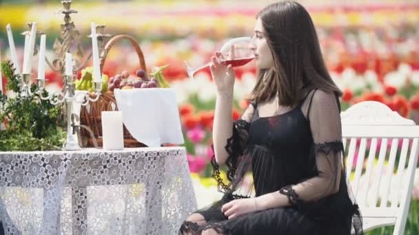 Девушка пьет вино сидя за столом — стоковое видео