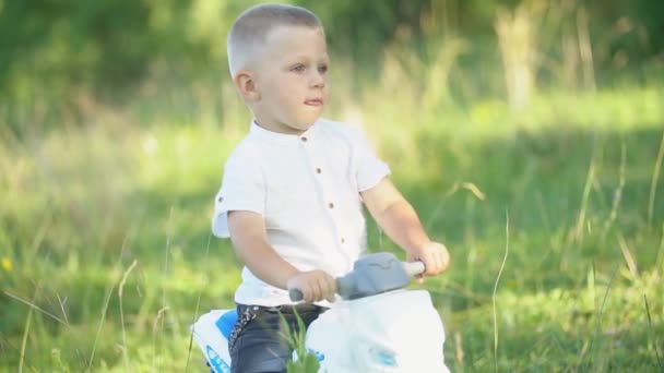 Niño se sienta en una bicicleta de plástico — Vídeo de stock