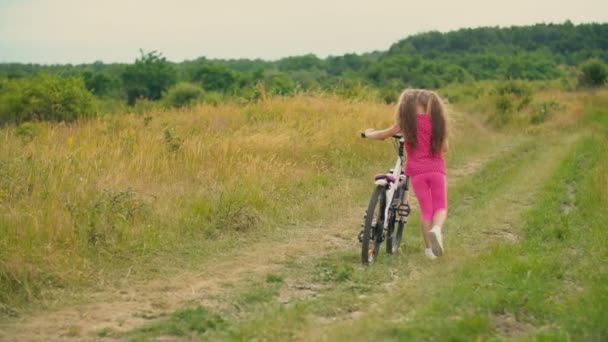 Liten flicka med en cykel i naturen — Stockvideo