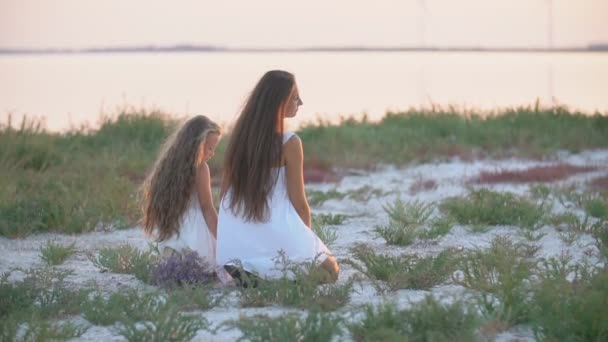 Mamá y su hija se sientan en la playa y miran a la distancia — Vídeos de Stock