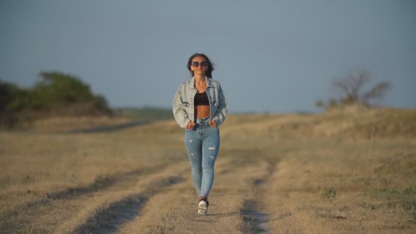 Meisje in jeans wandelingen langs de weg — Stockvideo