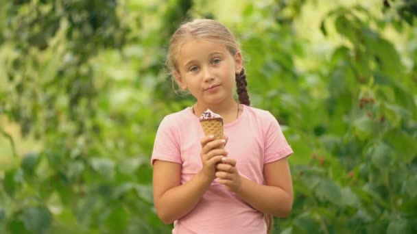 Mädchen isst Eis auf einem Hintergrund aus grünem Laub — Stockvideo