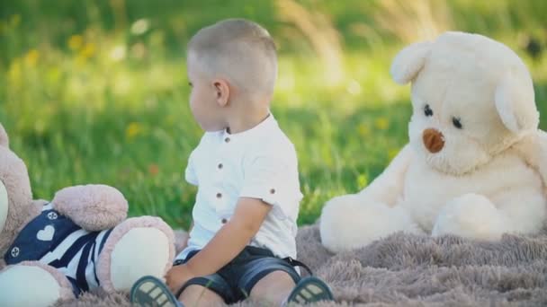 Kleiner Junge sitzt auf einer Decke mit Teddybären — Stockvideo