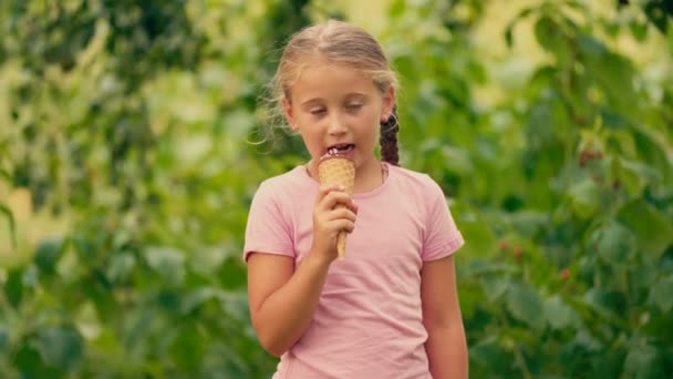 Niña comiendo helado sobre un fondo de follaje verde — Vídeos de Stock