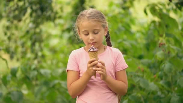 Girl eating ice cream on a background of green foliage — Stock Video