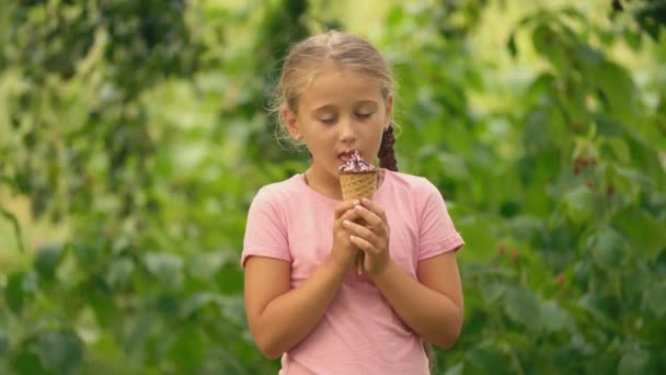 Mädchen isst Eis auf einem Hintergrund aus grünem Laub — Stockvideo