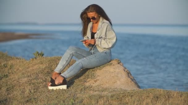Девушка в солнечных очках смотрит в телефон — стоковое видео