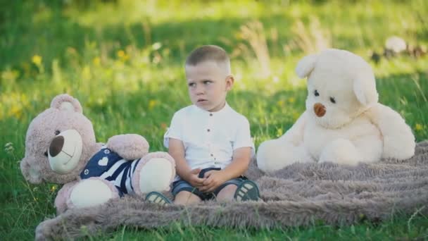 Kleiner Junge sitzt auf einer Decke mit Teddybären — Stockvideo