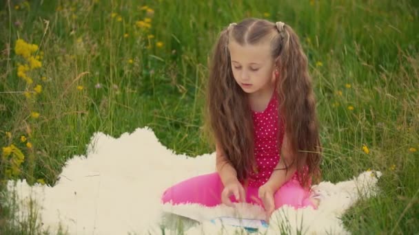 Девушка читает книгу, сидя на лужайке — стоковое видео