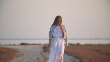 elinde çiçek ile kız kumlu bir yolda gider