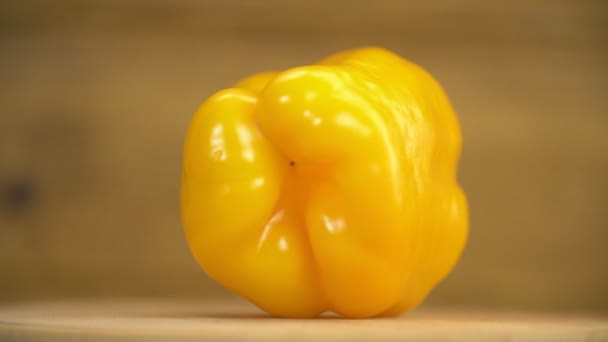 Κίτρινη πιπεριά που περιστρέφεται σε ξύλινο τραπέζι — Αρχείο Βίντεο