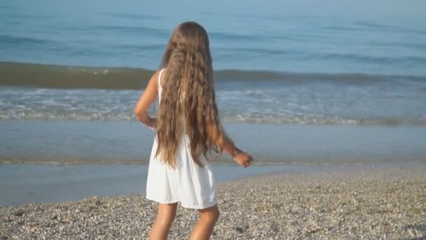 Klein meisje in een witte jurk wandelingen in de buurt van de zee — Stockvideo