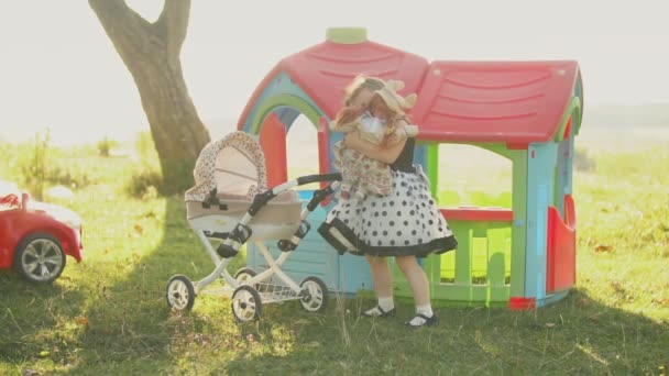 Kleines Mädchen spielt mit einer Puppe in der Nähe eines Spielzeugwagens — Stockvideo