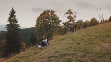 Çift bir tepede oturuyor ve uzaklığa bakıyor.