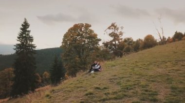 Çift bir tepede oturuyor ve uzaklığa bakıyor.