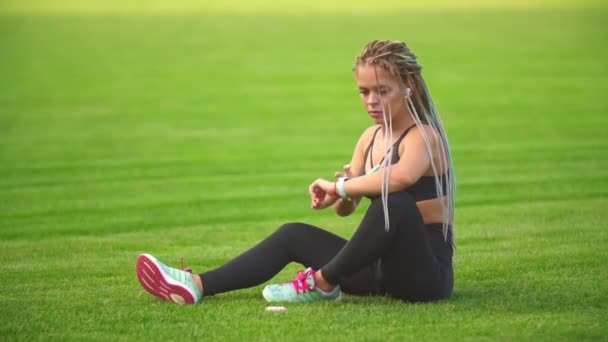 Dívka s telefonem sedí na trávníku — Stock video