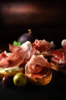 İtalyanca füme jambon kanepeler ile yeşil ve siyah zeytin ve fesleğen bitki kopya alanı için cömert konaklama ile siyah bir arka plan karşı atış garnitür.