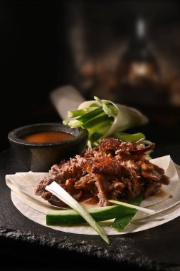 Creatively lit succulent classic Chinese shredded Peking duck with Hoisin sauce and flour pancakes with sliced scallions and cucumber garnish. Copy space. clipart