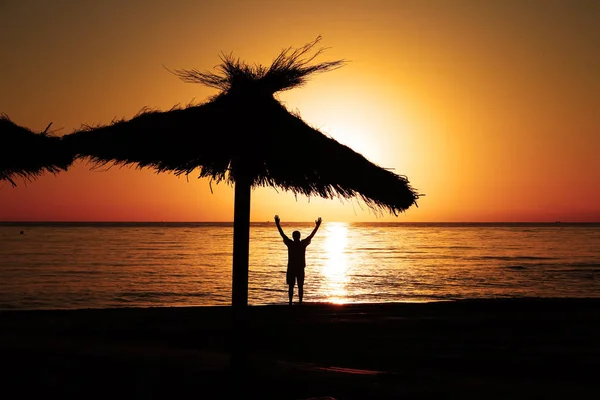 Ein Mann am Strand begrüßt den Sonnenaufgang mit erhobenen Händen. — Stockfoto
