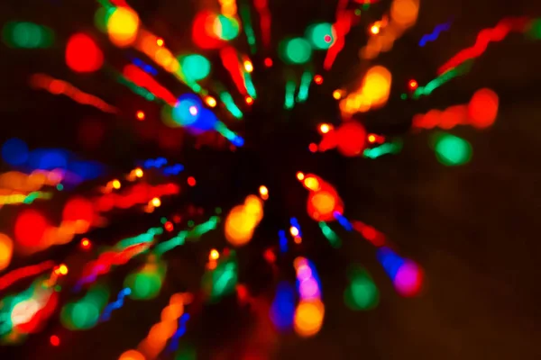 Festive mood from colorful lights in the dark. The effect of elegant bokeh from the lights of the Christmas garland. Shining sparks and burning paths fly to the sides from the center.