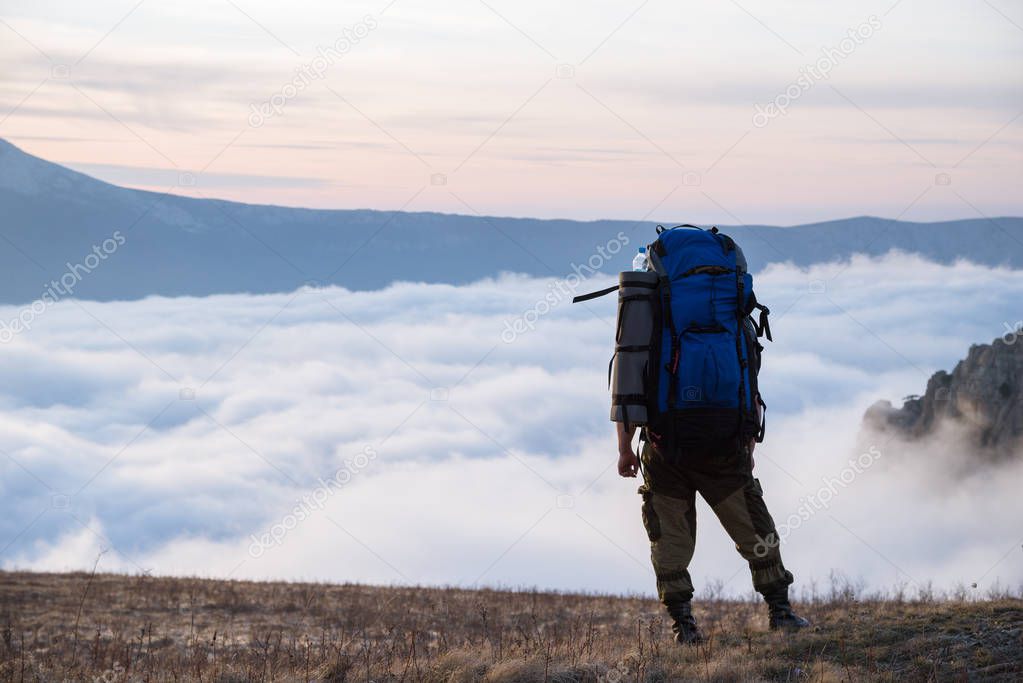 A tourist is standing in the mountains with a backpack and looking at the clouds. Demerdzhi, Crimea.