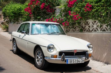 Santa Ponsa, Mallorca, İspanya - 24 Temmuz 2013: Retro araba Mg Bgt çiçekli bir duvarının yakınında park edilmiş ve palmiye yaprakları.