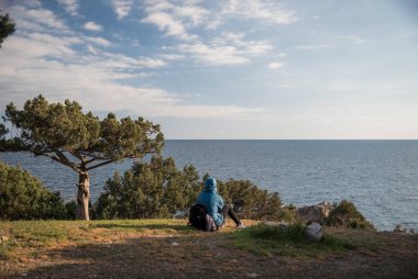 Foros, Kırım Cumhuriyeti - 1 Nisan 2019: Kırım yarımadasının güney kıyısında Karadeniz'in karşısındaki bir ağacın yanında çimenlerin üzerinde oturan turist