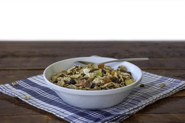 A bowl full of muesli cereals with spoon over a wooden table