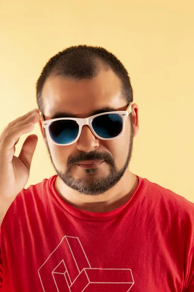 man with red shirt and white sunglasses over a yellow background.