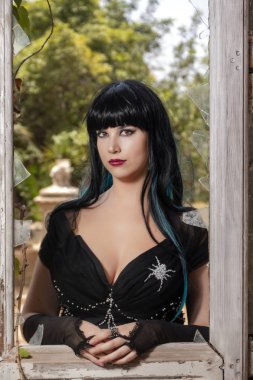 Terk edilmiş bir saray ahşap pencere yanında üzerinde Gotik kız karanlık bir görünümünü giyinmiş.