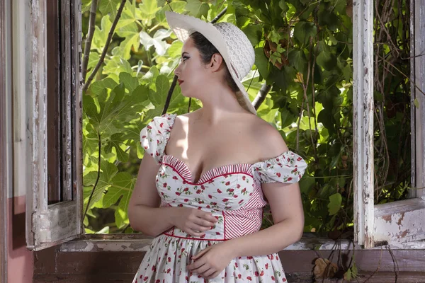 看到一个乡村的年轻淑女妇女与白色的礼服和红色的花朵和帽子在一个废弃的宫殿旁边的窗口 — 图库照片