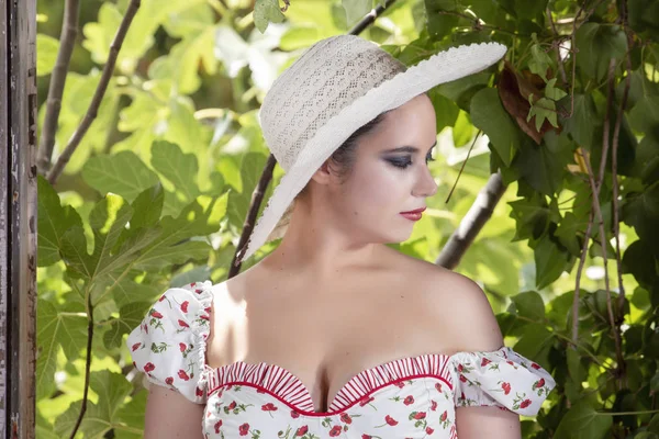 一个农村年轻女士的视图白色的礼服和红色的花朵和帽子在废弃的宫殿对无花果树枝 — 图库照片