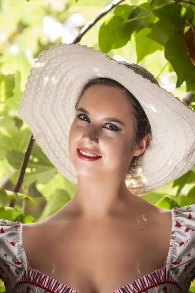 イチジクの木の枝に対して放棄された宮殿で白いドレスと赤い花と帽子の田舎の若い女性の女性観 — ストック写真