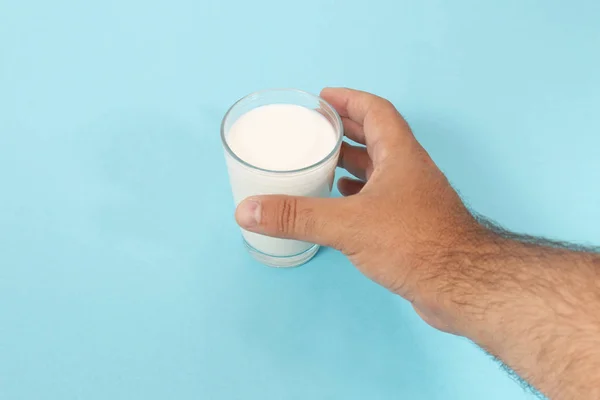 hand grabs glass of milk on a blue background.