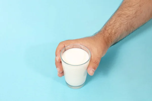 hand grabs glass of milk on a blue background.
