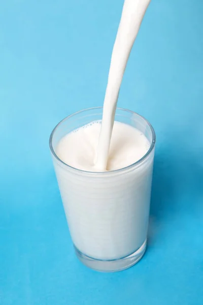 Verter Leche Sobre Vaso Aislado Sobre Fondo Azul —  Fotos de Stock