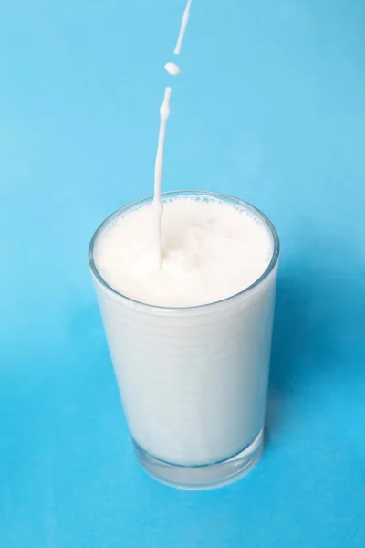 Verter Leche Sobre Vaso Aislado Sobre Fondo Azul —  Fotos de Stock