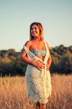 Kırsalda bikinili bir kadın, kuru otların üzerinde şık bir yaşam tarzında poz veriyor..