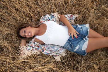 Kırsalda poz veren güzel bir kız kuru çimlerin üzerinde kısa kot pantolonla.