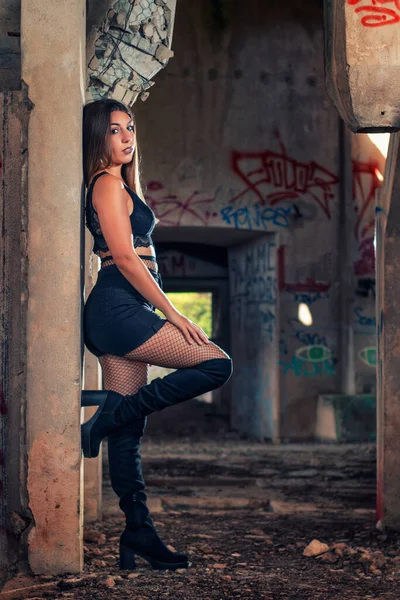 若いです女の子Posingでファッション方法でA放棄された工場の建物を使用して黒トップと短いジーンズとスリックブラックブーツ — ストック写真