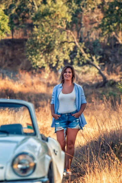有一辆白色可兑换古董车的妇女在乡间行走 — 图库照片