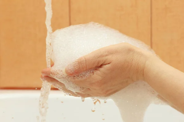 Female hands with foam under the jet of water in the bathroom